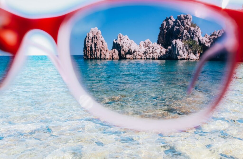 Looking through one lens of polarized sunglasses showing improved clarity and colour perception of big jutting out rocks in the water.