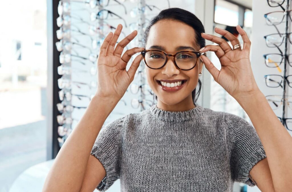 A smiling person puts on their new stylish glasses at their optometrist.