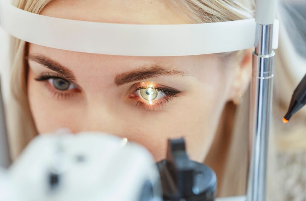 A person sits in front of a slit lamp while an optometrist examines the interior of their eye.