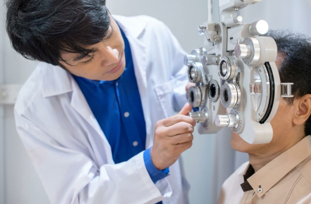 A patient sits behind a phoropter while an optometrist adjusts the knobs to determine the patient's glasses prescription.